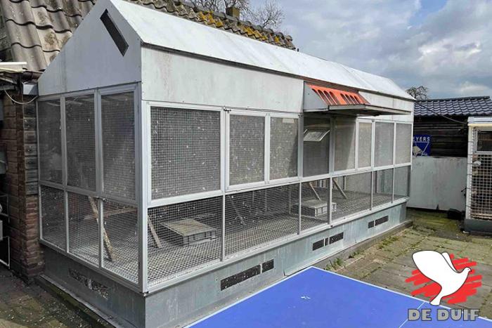 Hok van de overjarige vliegers met volière waarvan de bovenkant is afgeschermd met on- doorzichtige platen. Het bovenste deel van de voor- en zijkant bestaat uit windbreekgaas en de onderste 60 cm is open.